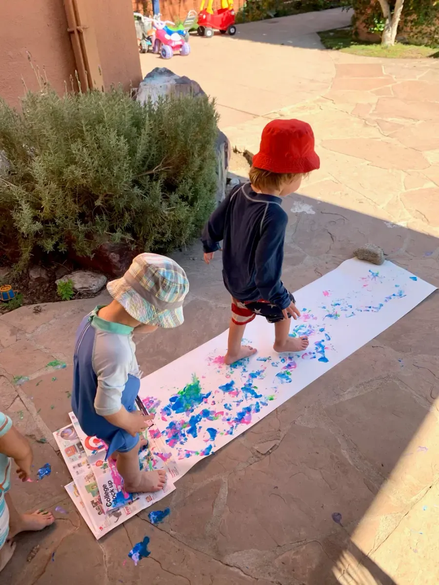 Toddlers painting on a long paper roll outside