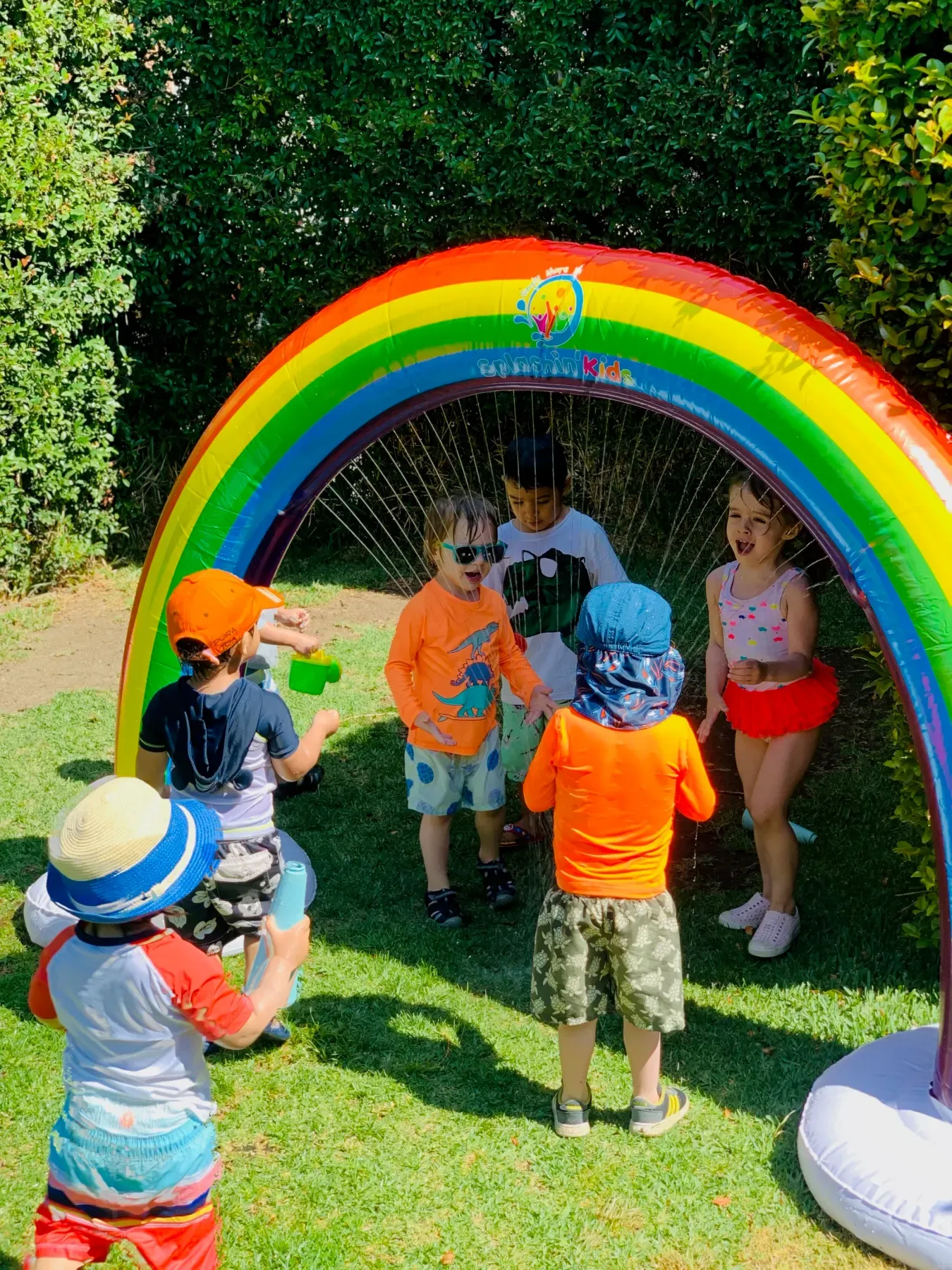 Kids running under a rainbow sprinkler arch