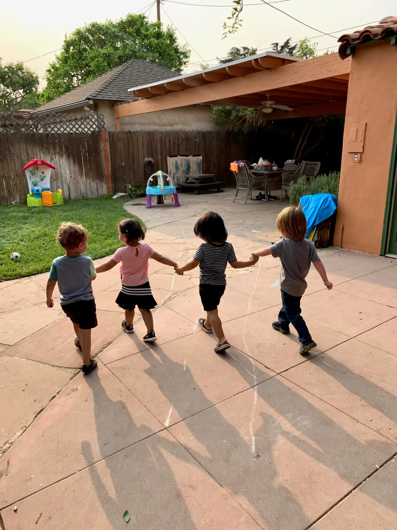 Four toddlers holding hands as they run across the patio