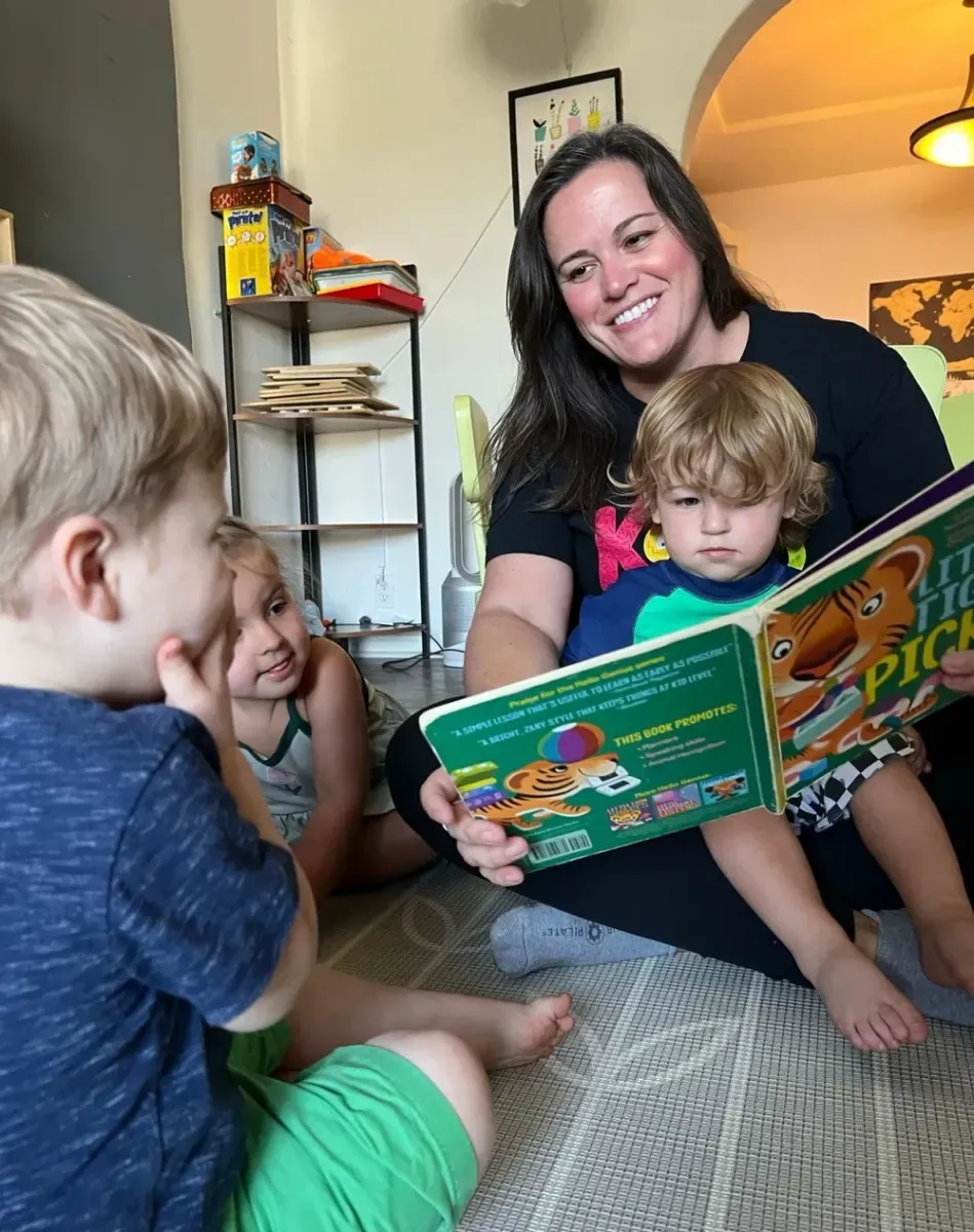 A caregiver reading a picture book with two toddlers